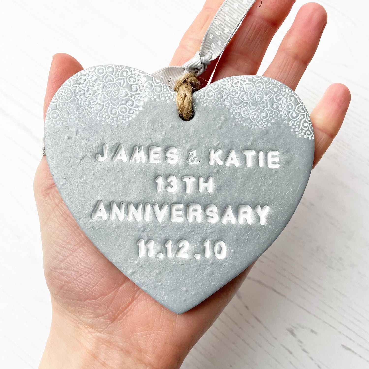 Personalised anniversary gift, silver clay heart with a white lace edge at the top of the heart with jute twine for hanging, the heart is personalised with JAMES & KATIE 13TH ANNIVERSARY 11.12.10