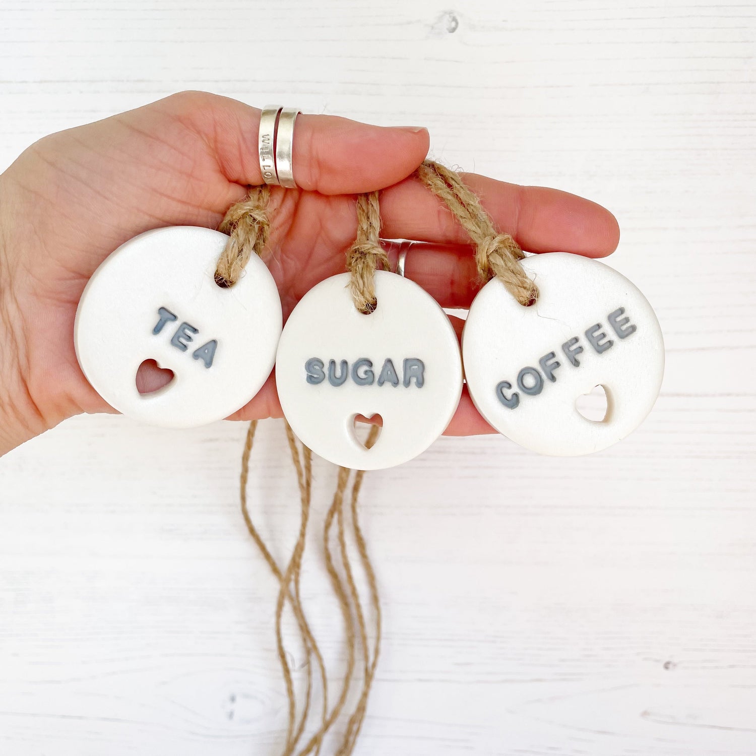 3 round pearlised white clay kitchen canister labels with a small heart cut out at the bottom, with coffee, tea and sugar stamped on each label