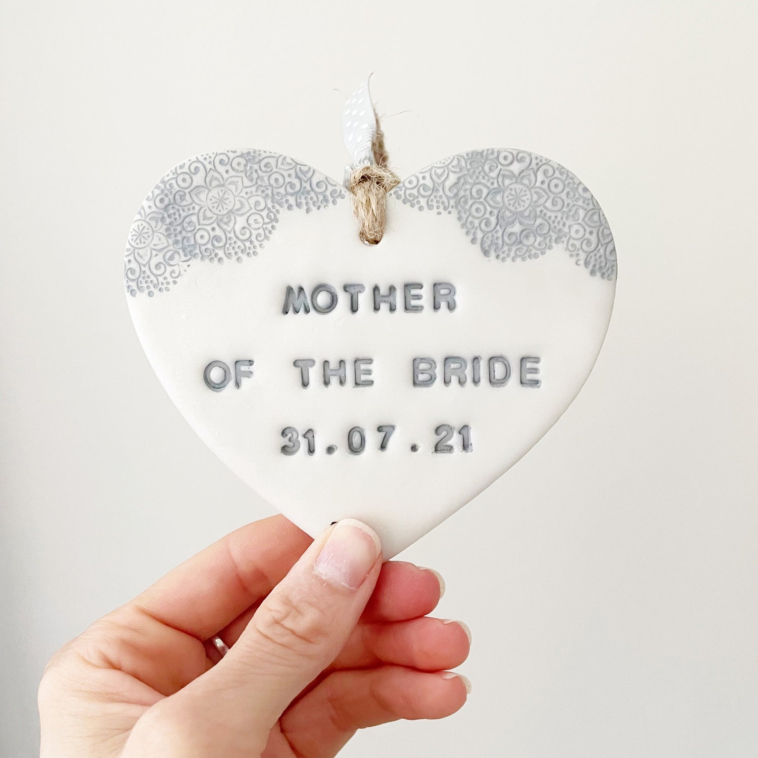 Personalised Bridesmaid thank you gift, pearlised white clay hanging heart with a grey lace edge at the top of the heart, the heart is personalised with MOTHER OF THE BRIDE 31.07.21
