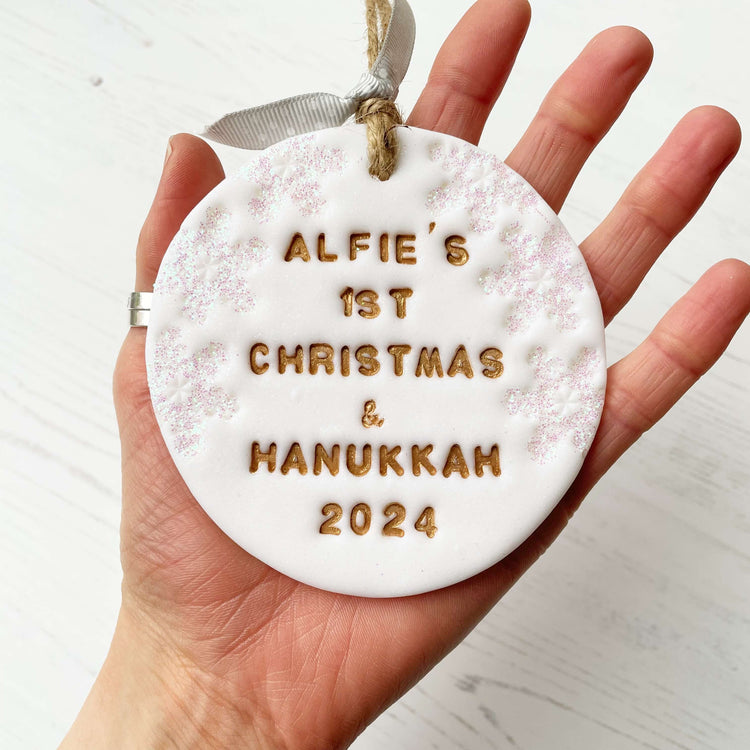 Personalised baby's first Christmas bauble ornament, pearlised white round clay with PIPPA’S FIRST CHRISTMAS 2023 in grey paint, decorated with 3 iridescent glitter snowflakes on either side of the bauble