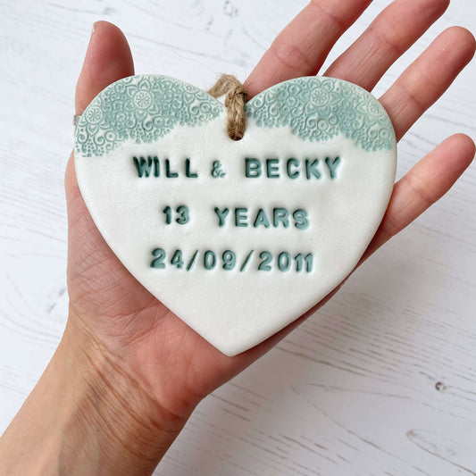 Personalised 13th anniversary gift, pearlised white clay hanging heart with a safe green lace edge at the top of the heart, the heart is personalised with WILL & BECKY 13 YEARS 24/09/2011