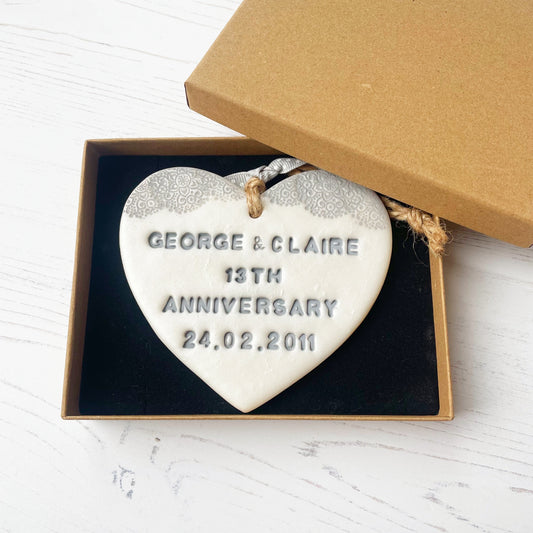 Personalised 13th anniversary gift, pearlised white clay hanging heart with a grey lace edge at the top of the heart, the heart is personalised with GEORGE & CLAIRE 13TH ANNIVERSARY 24.02.2011 in a luxury brown Kraft gift box