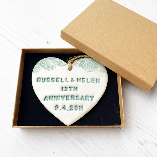 Personalised 13th wedding anniversary gift, pearlised white clay hanging heart with a sage green lace edge at the top of the heart, the heart is personalised with RUSSELL& HELEN 13TH ANNIVERSARY 9.4.2011