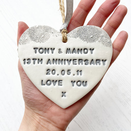 Personalised 13th anniversary gift, pearlised white clay hanging heart with a grey lace edge at the top of the heart, the heart is personalised with TONY & MANDY 13TH ANNIVERSARY 20.05.11 LOVE YOU X