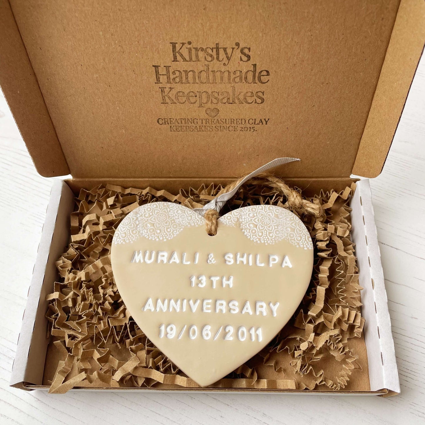 Personalised 13th anniversary gift, beige clay heart with a white lace edge at the top of the heart with jute twine for hanging, the heart is personalised with MURALI & SHILPA 13TH ANNIVERSARY 19/06/2011