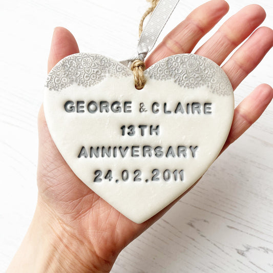 Personalised 13th anniversary gift, pearlised white clay hanging heart with a grey lace edge at the top of the heart, the heart is personalised with GEORGE & CLAIRE 13TH ANNIVERSARY 24.02.2011