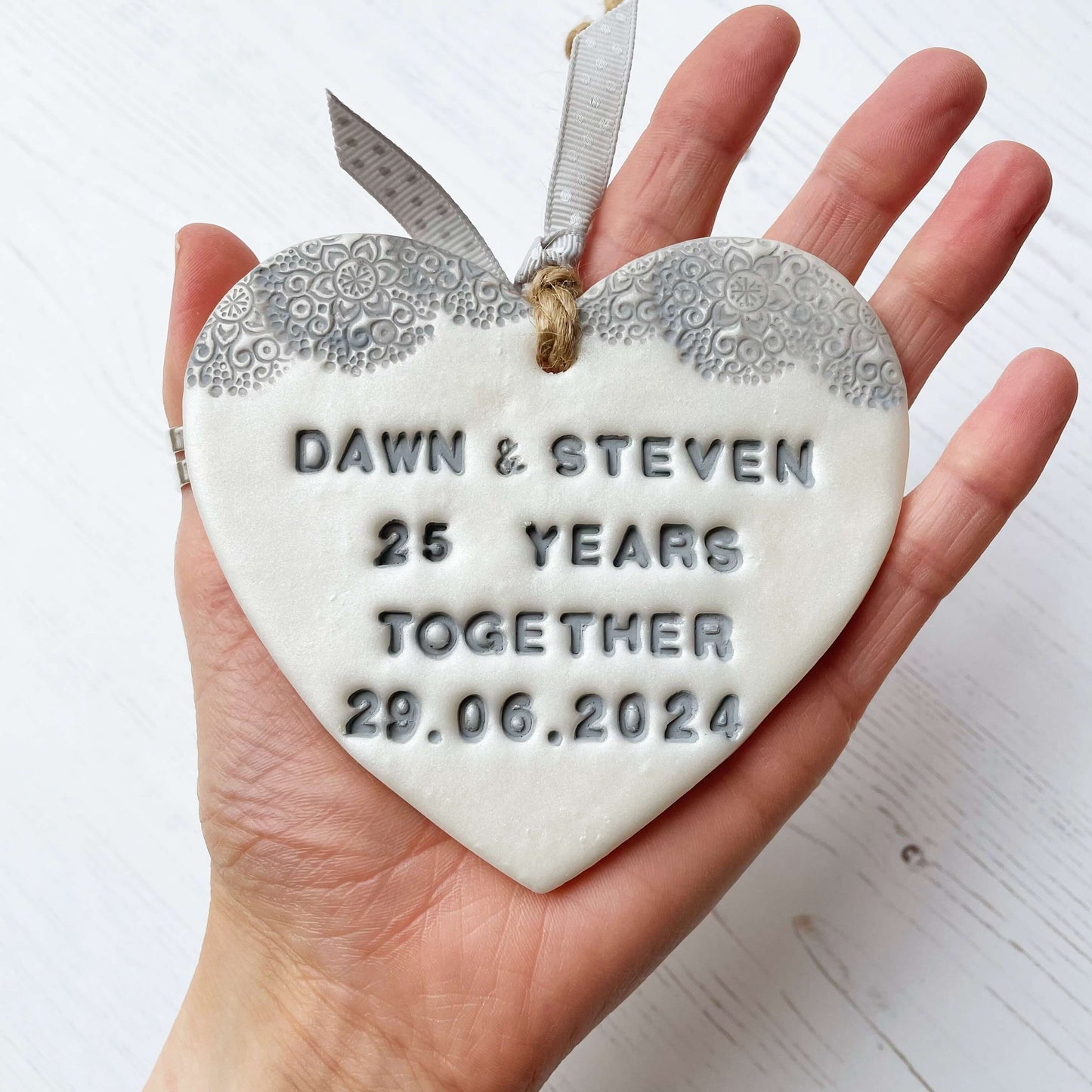 Personalised 25th anniversary gift, pearlised white clay hanging heart with a grey lace edge at the top of the heart, the heart is personalised with DAWN & STEVEN 25 YEARS TOGETHER 29.06.2024