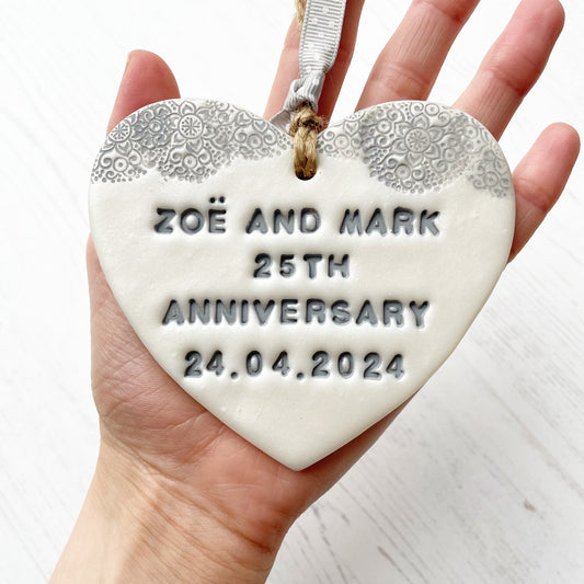 Personalised 25th anniversary gift, pearlised white clay hanging heart with a grey lace edge at the top of the heart, the heart is personalised with ZOË AND MARK 25TH ANNIVERSARY 24.04.2024