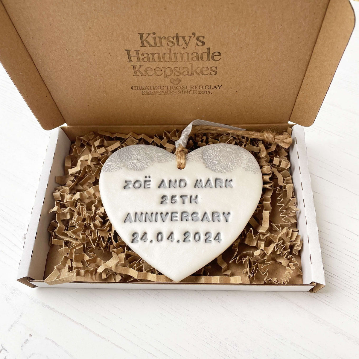 Personalised 25th anniversary gift, pearlised white clay hanging heart with a grey lace edge at the top of the heart, the heart is personalised with ZOË AND MARK 25TH ANNIVERSARY 24.04.2024