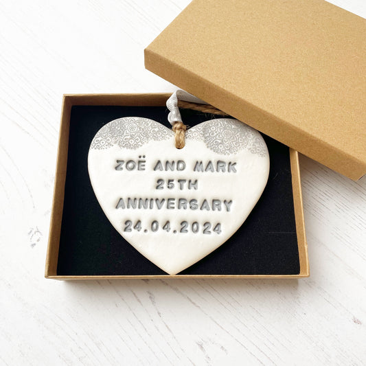 Personalised 25th anniversary gift, pearlised white clay hanging heart with a grey lace edge at the top of the heart, the heart is personalised with ZOË AND MARK 25TH ANNIVERSARY 24.04.2024 In a brown Kraft luxury gift box