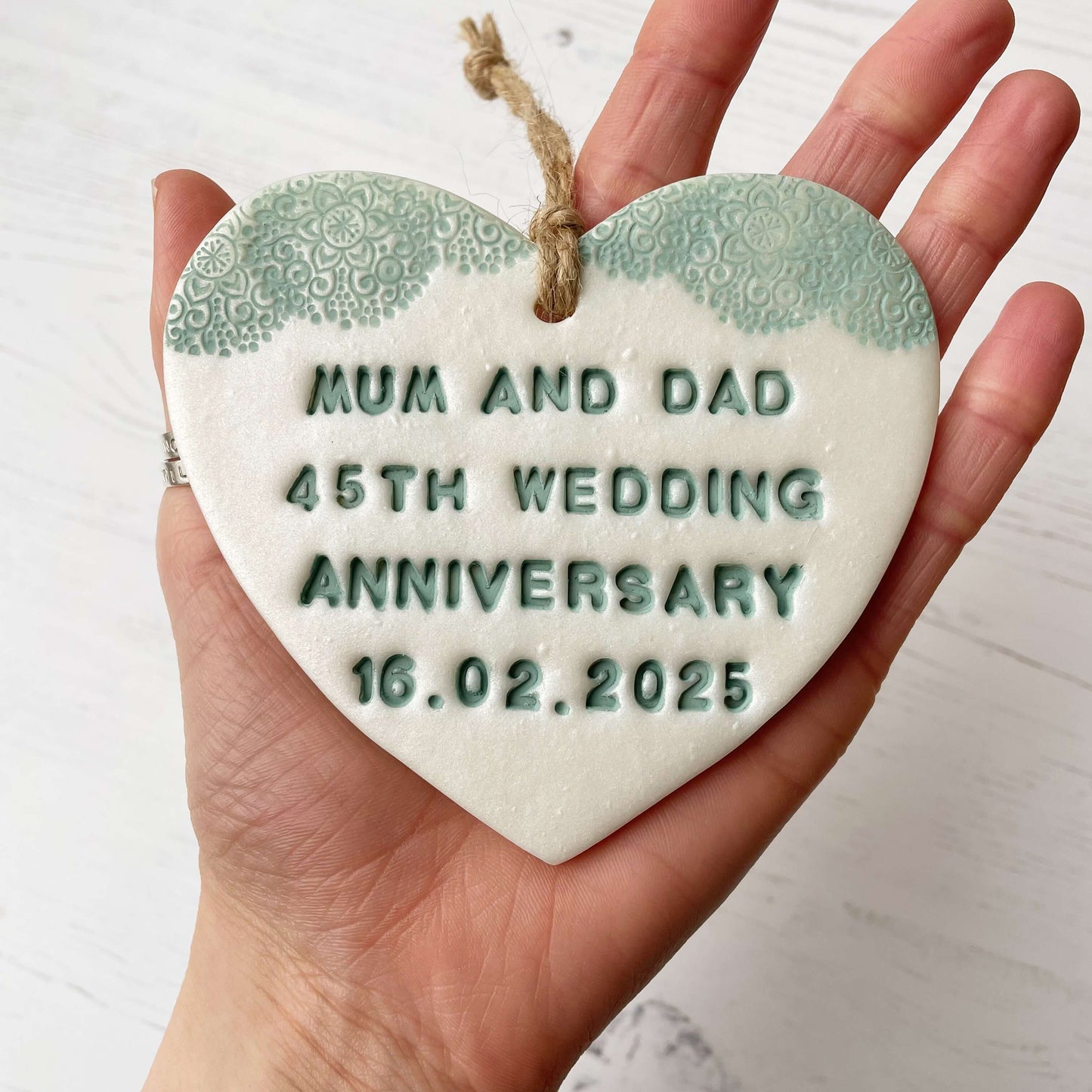 Personalised 45th anniversary gift, pearlised white clay hanging heart with a sage green lace edge at the top of the heart, the heart is personalised with MUM AND DAD 45TH WEDDING ANNIVERSARY 16.02.2025