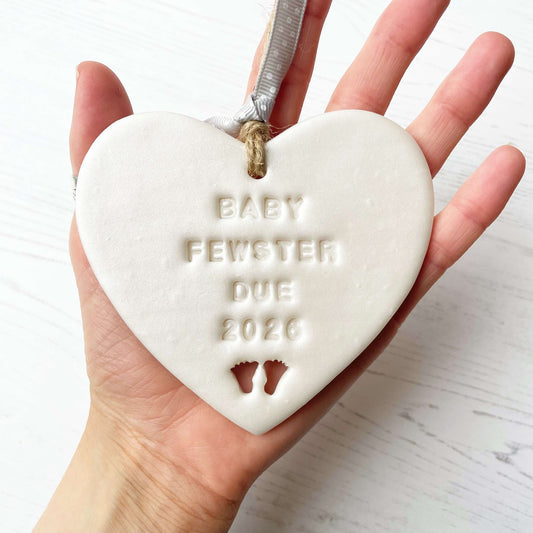 Personalised baby reveal gift, pearlised white clay heart with feet cut out of the bottom personalised with BABY FEWSTER DUE 2026