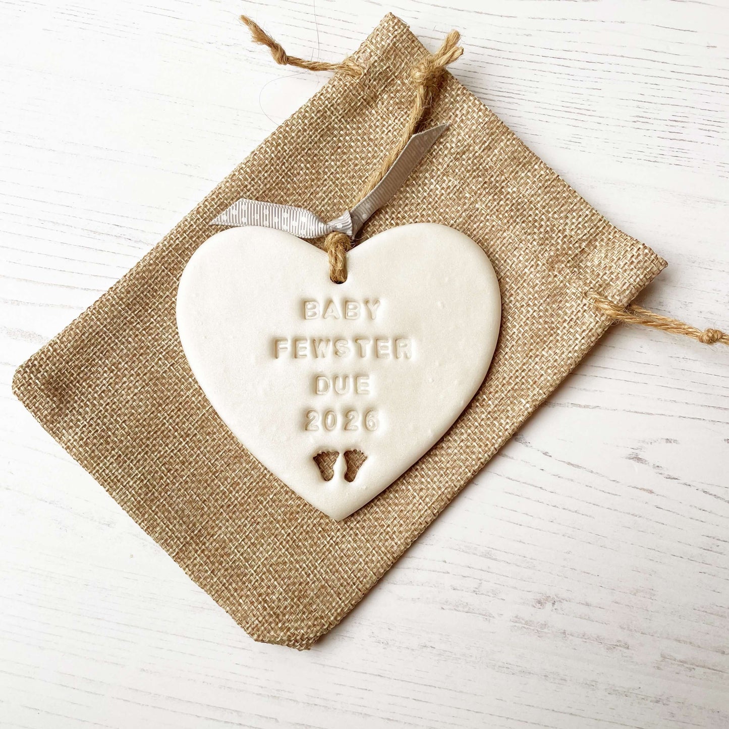 Personalised baby reveal gift, pearlised white clay heart with feet cut out of the bottom personalised with BABY FEWSTER DUE 2026