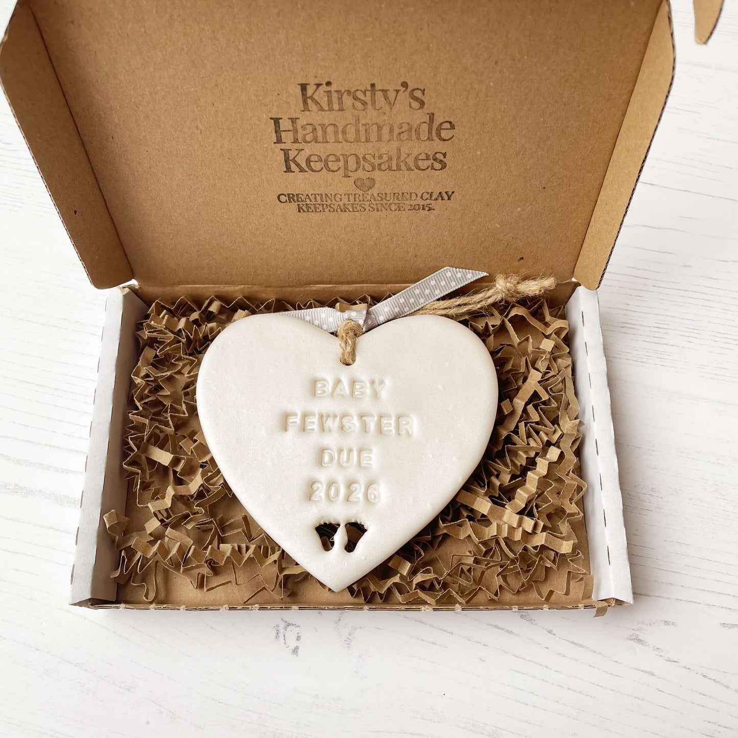 Personalised baby reveal gift, pearlised white clay heart with feet cut out of the bottom personalised with BABY FEWSTER DUE 2026