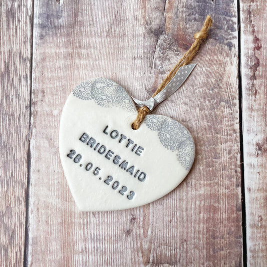 Personalised Bridesmaid thank you gift, pearlised white clay hanging heart with a grey lace edge at the top of the heart, the heart is personalised with LOTTIE BRIDESMAID 28.05.2023