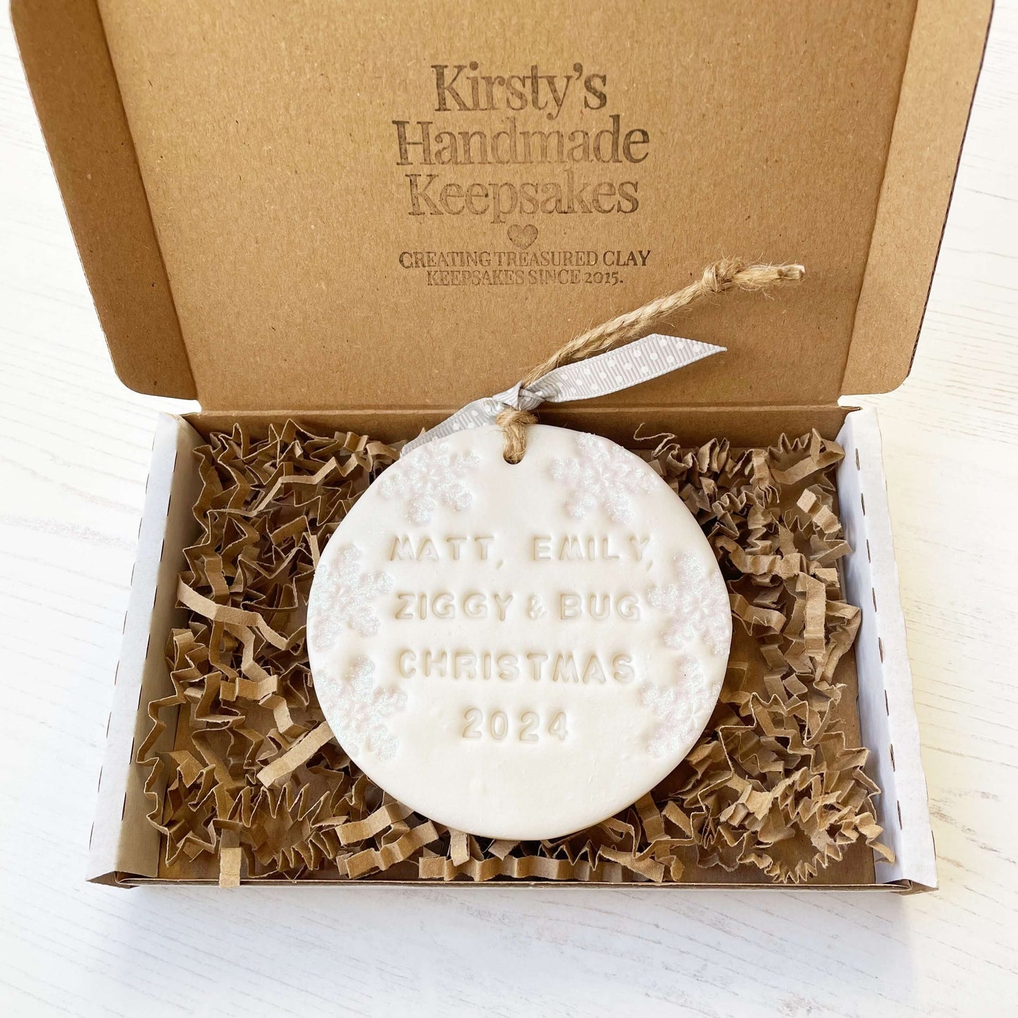 Personalised bump’s first Christmas bauble ornament, pearlised white round clay with MATT, EMILY, ZIGGY & BUG CHRISTMAS 2024, decorated with 3 iridescent glitter snowflakes on either side of the bauble