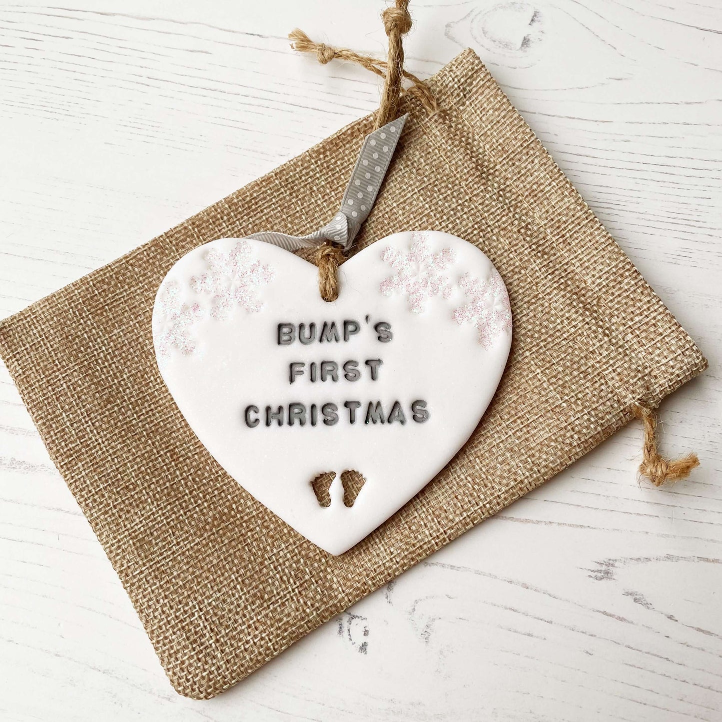 Personalised bump’s first Christmas heart ornament, glitter white clay with BUMP’S FIRST CHRISTMAS painted grey, decorated with 2 iridescent glitter snowflakes on either side of the top of the heart and baby feet cut out at the bottom