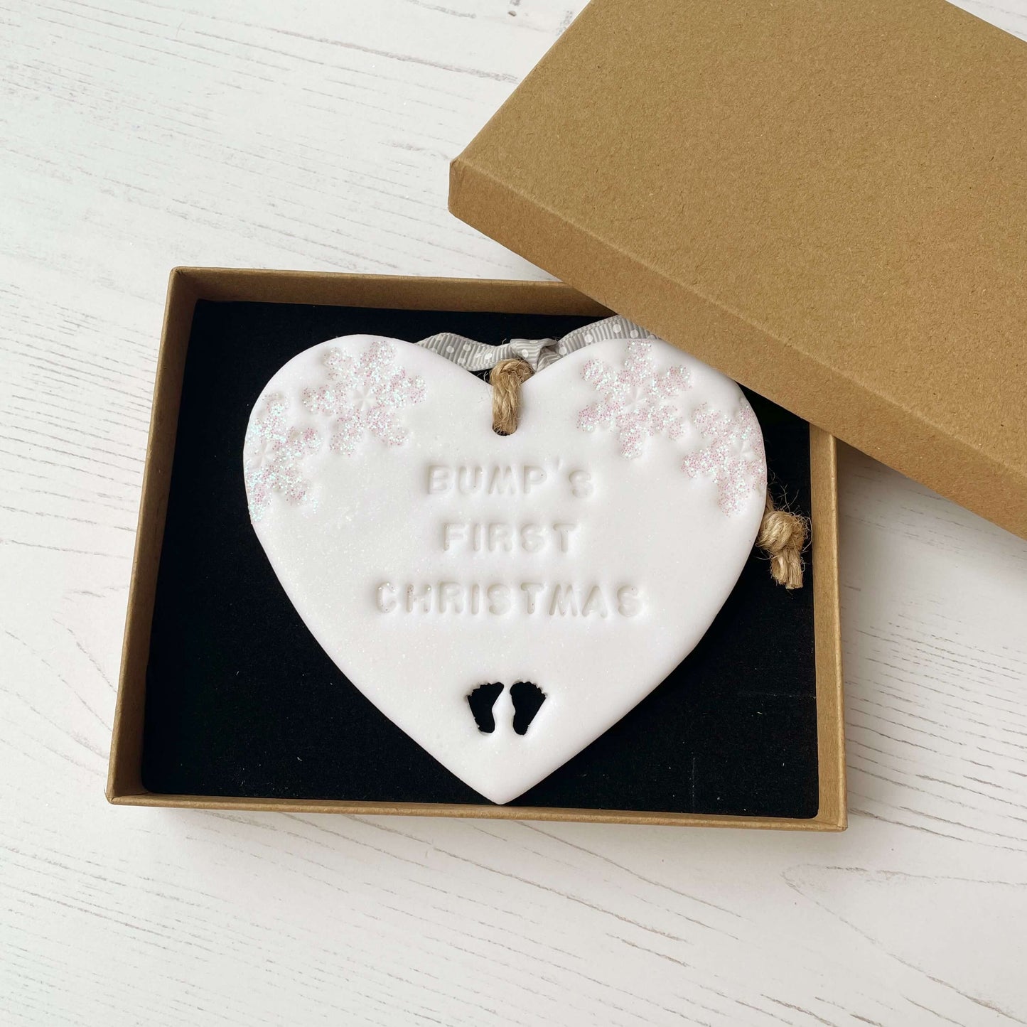 Personalised bump’s first Christmas heart ornament, glitter white clay with BUMP’S FIRST CHRISTMAS, decorated with 2 iridescent glitter snowflakes on either side of the top of the heart and baby feet cut out at the bottom