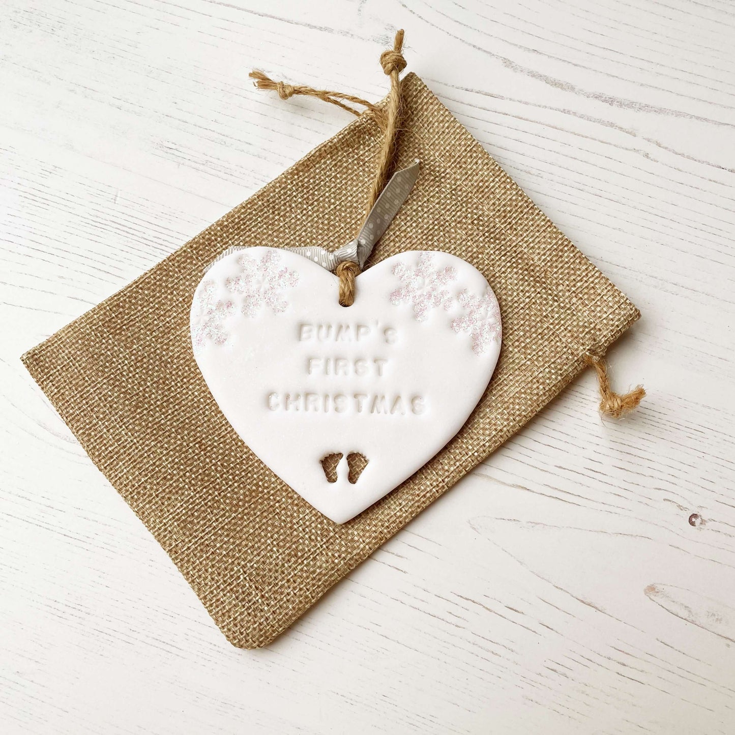 Personalised bump’s first Christmas heart ornament, glitter white clay with BUMP’S FIRST CHRISTMAS, decorated with 2 iridescent glitter snowflakes on either side of the top of the heart and baby feet cut out at the bottom