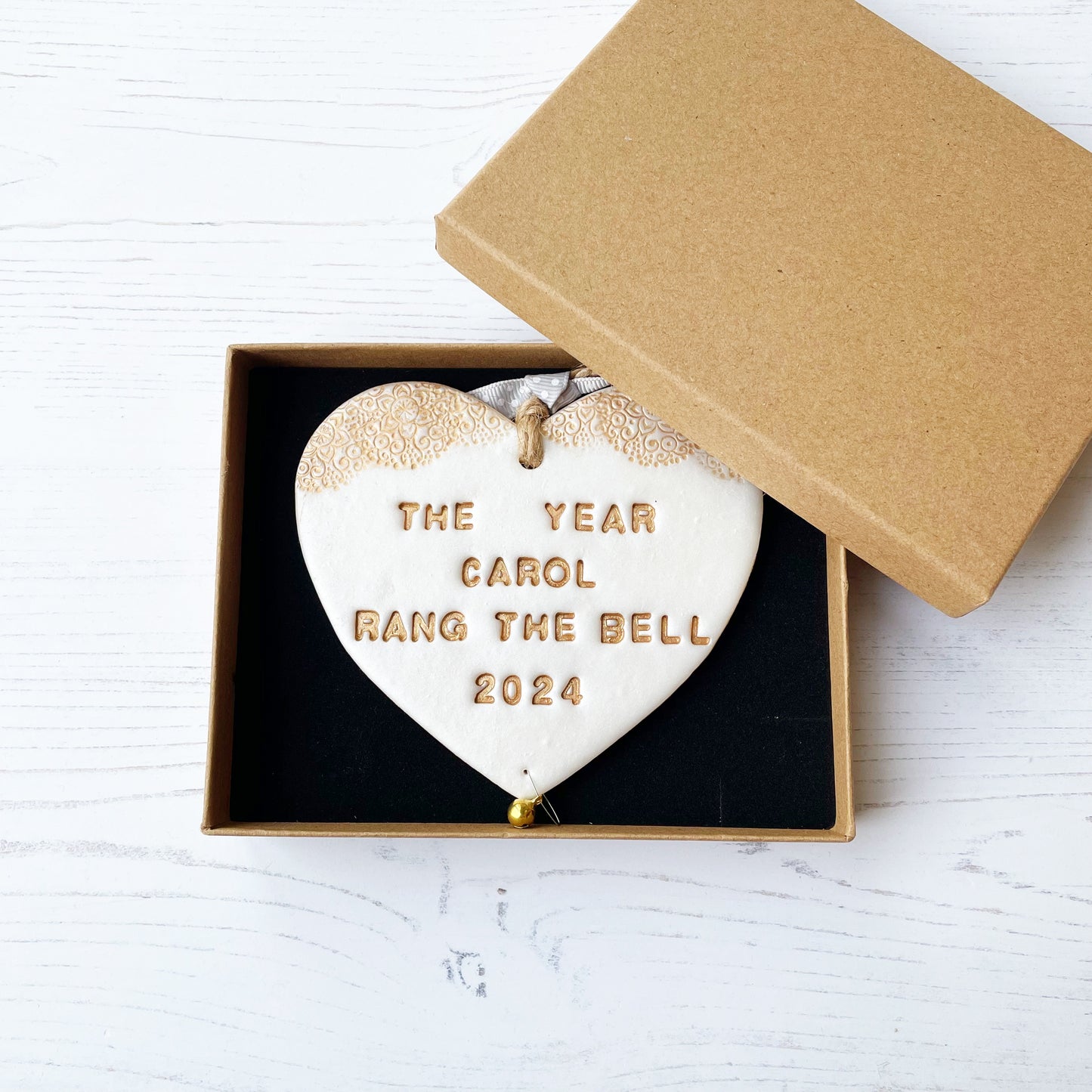 Personalised cancer survivor gift, pearlised white clay hanging heart with a gold lace edge at the top of the heart and a gold bell hanging below, the heart is personalised with THE YEAR CAROL RANG THE BELL 2024. In a luxury Kraft brown gift box
