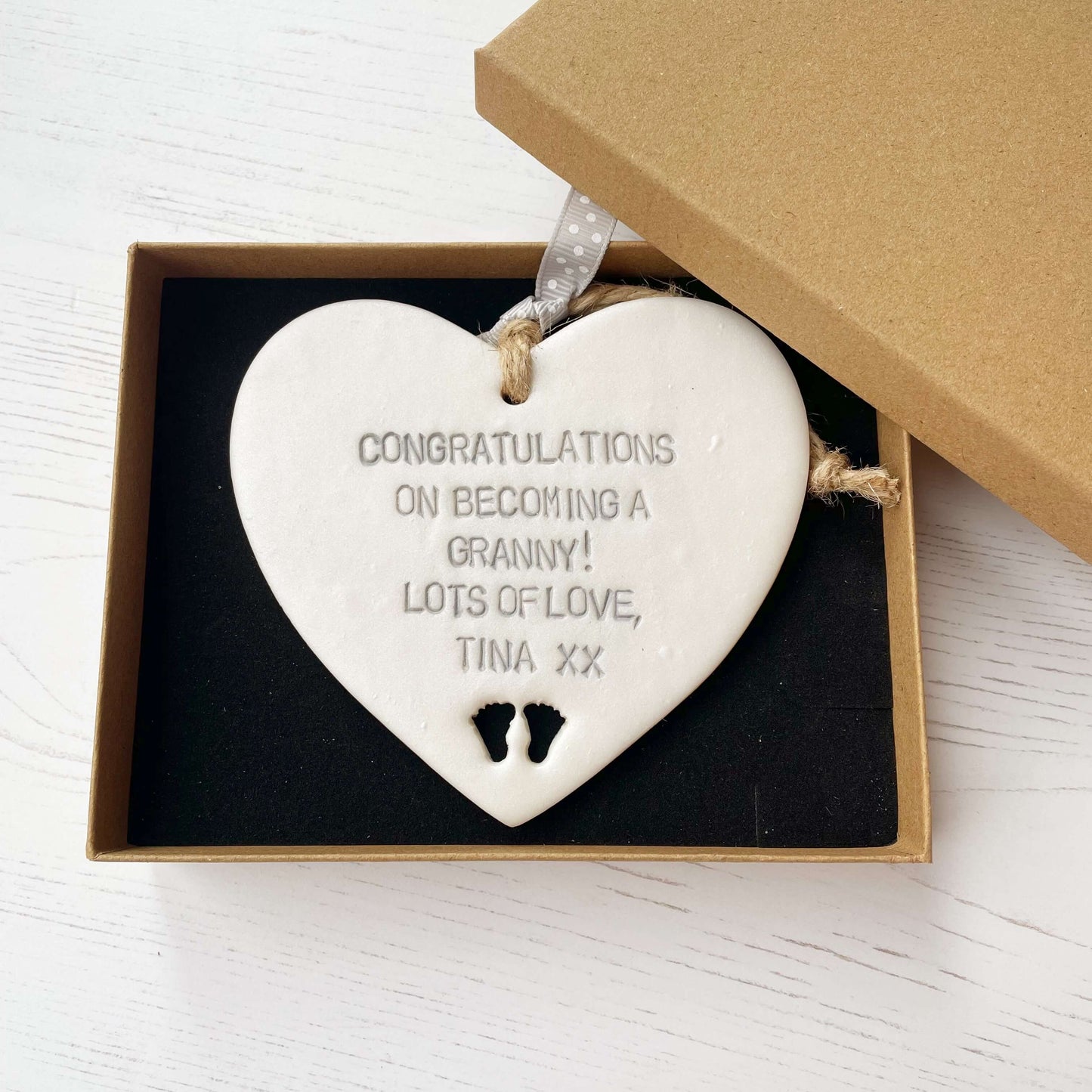 Pearlised white clay hanging heart with baby feet cut out of the bottom and grey personalisation, the heart is personalised with CONGRATULATIONS ON BECOMING A GRANNY! LOTS OF LOVE TINA XX