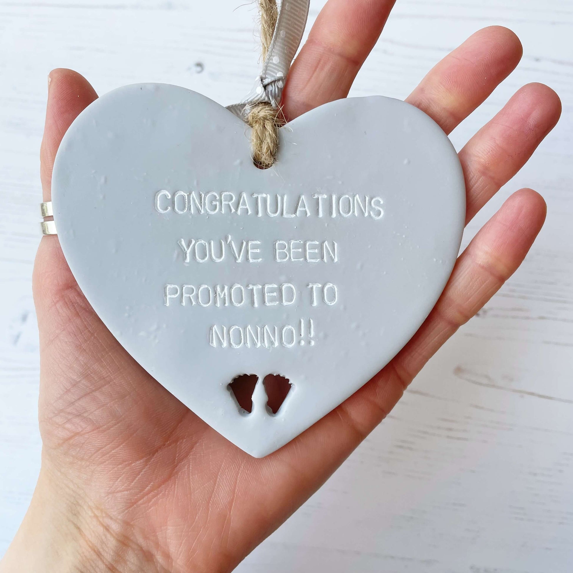 Grey clay hanging heart with baby feet cut out of the bottom and white personalisation, the heart is personalised with CONGRATULATIONS YOU’VE BEEN PROMOTED TO NONNO!!