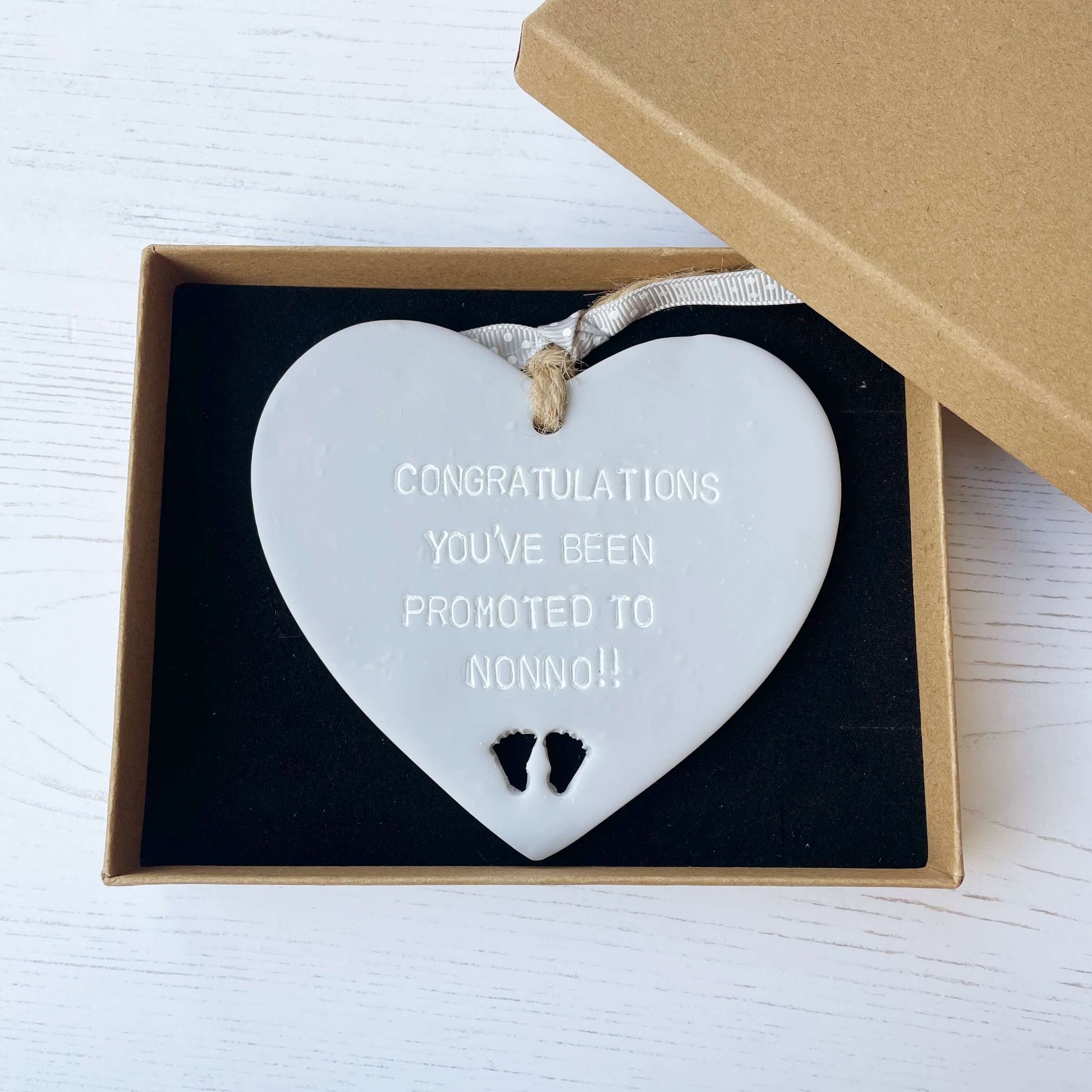 Grey clay hanging heart with baby feet cut out of the bottom and white personalisation, the heart is personalised with CONGRATULATIONS YOU’VE BEEN PROMOTED TO NONNO!!