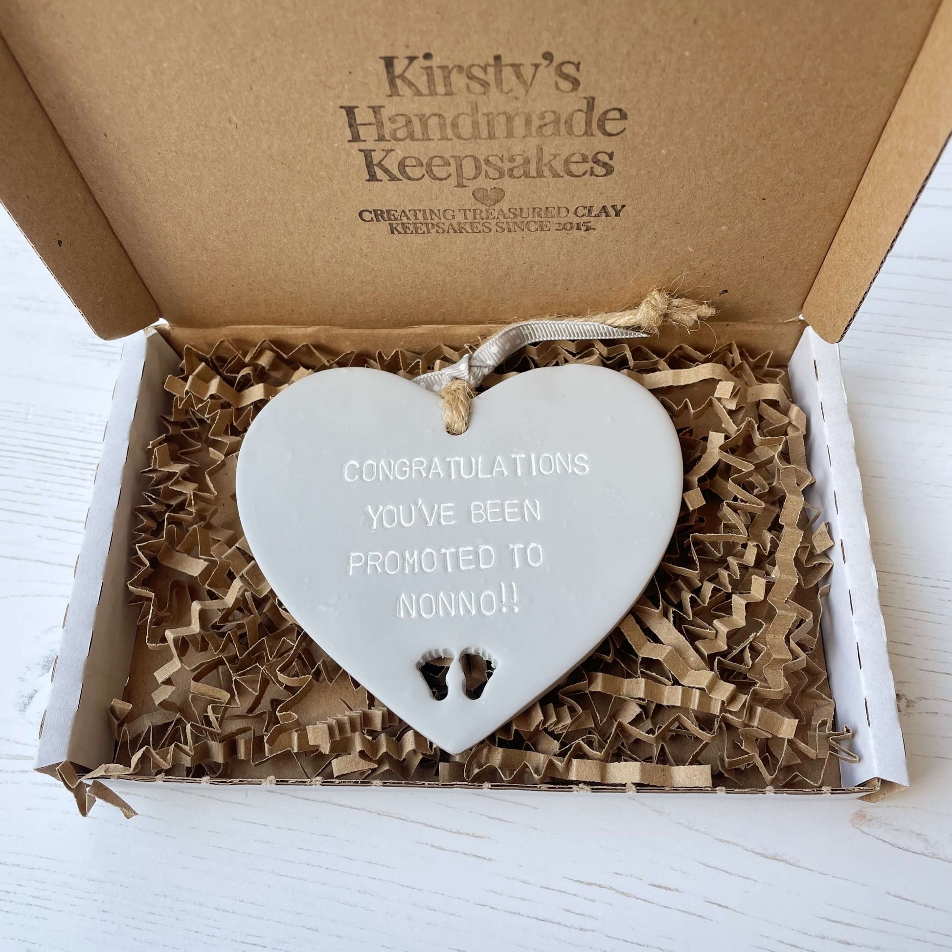Grey clay hanging heart with baby feet cut out of the bottom and white personalisation, the heart is personalised with CONGRATULATIONS YOU’VE BEEN PROMOTED TO NONNO!!