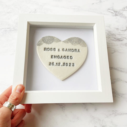 Personalised framed engagement gift, pearlised white clay heart with a white lace edge at the top of the heart in a white box frame, the heart is personalised with ROSS & SANDRA ENGAGED 26.12.2023