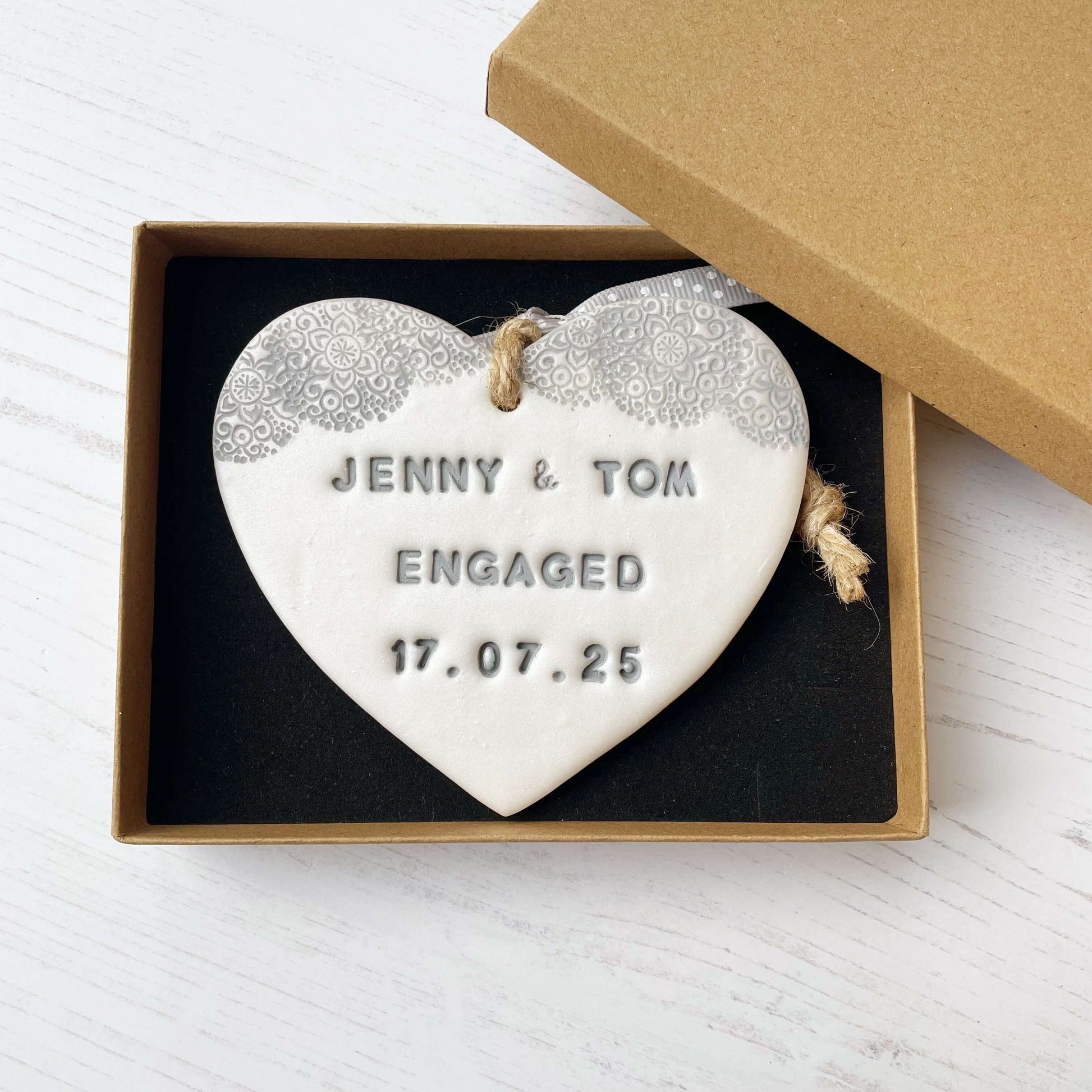 Personalised wedding gift, pearlised white clay hanging heart with a grey lace edge at the top of the heart, the heart is personalised with JENNY & TOM ENGAGED 17.07.25