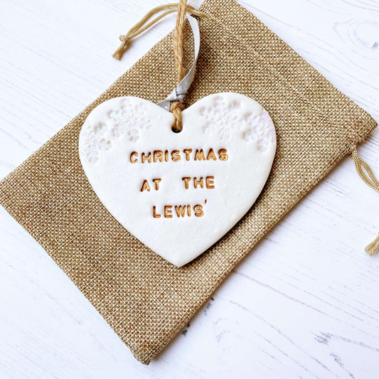 Personalised family Christmas heart ornament, pearlised white clay with CHRISTMAS AT THE LEWIS’ painted gold, decorated with 2 iridescent glitter snowflakes on either side of the top of the heart