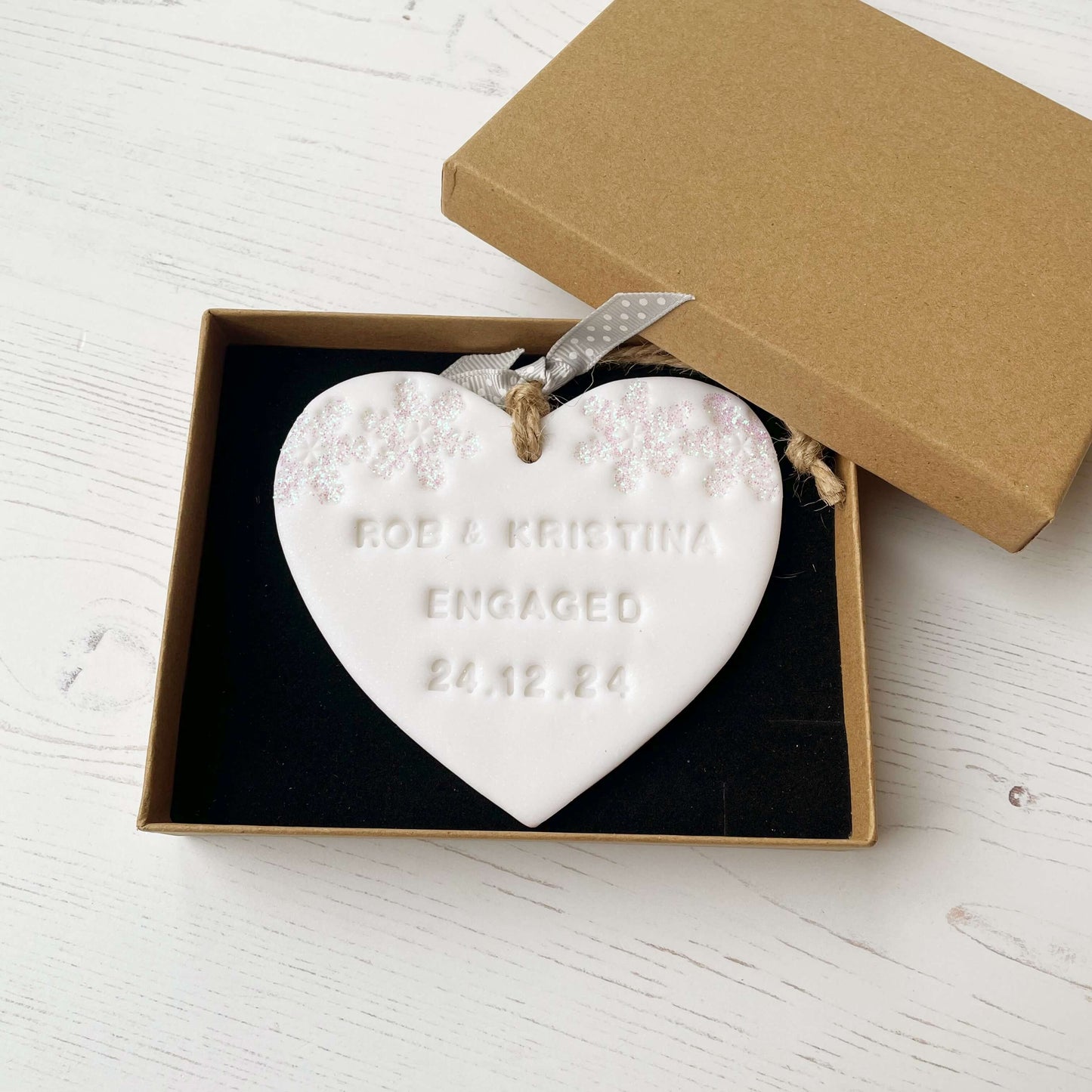 Personalised first Christmas engaged heart ornament, glitter white clay with ROB & KRISTINA ENGAGED 24.12.24 (text not painted), decorated with 2 iridescent glitter snowflakes on either side of the top of the heart