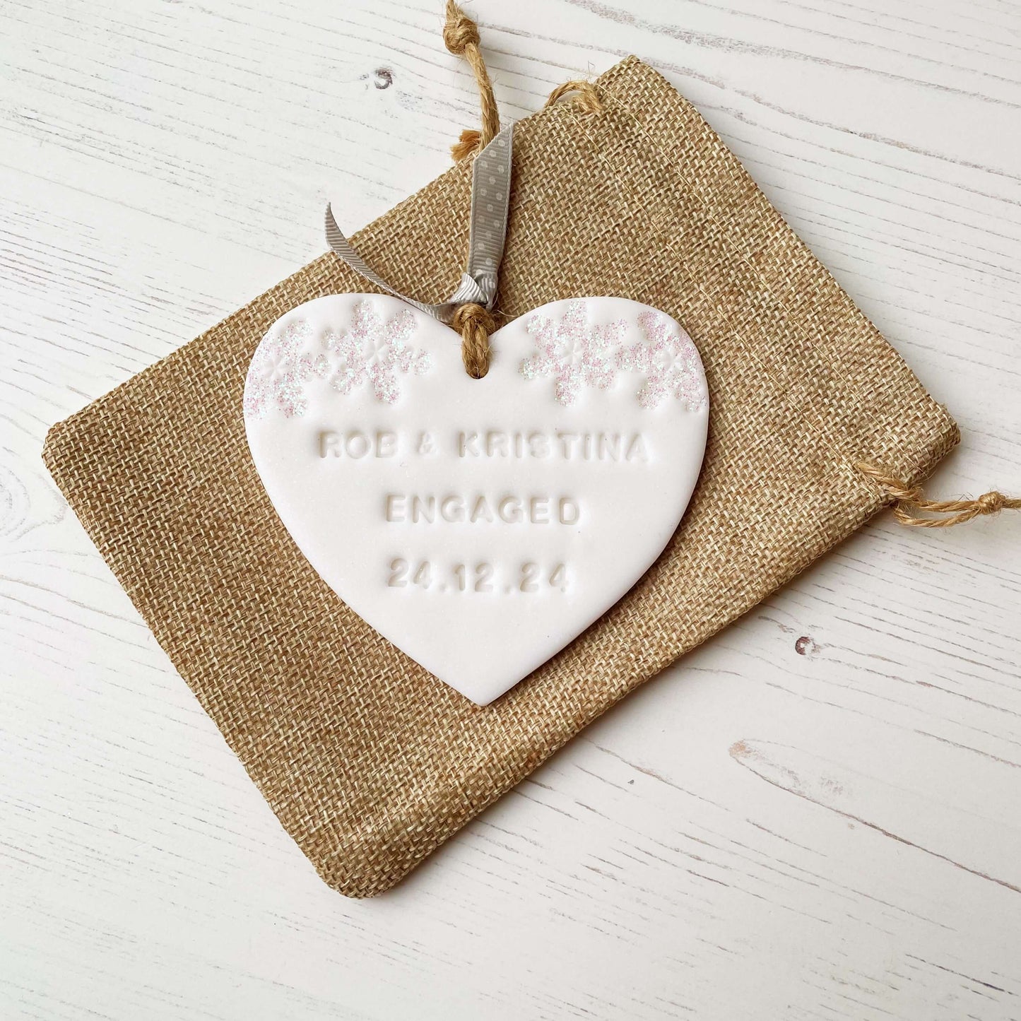 Personalised first Christmas engaged heart ornament, glitter white clay with ROB & KRISTINA ENGAGED 24.12.24 (text not painted), decorated with 2 iridescent glitter snowflakes on either side of the top of the heart