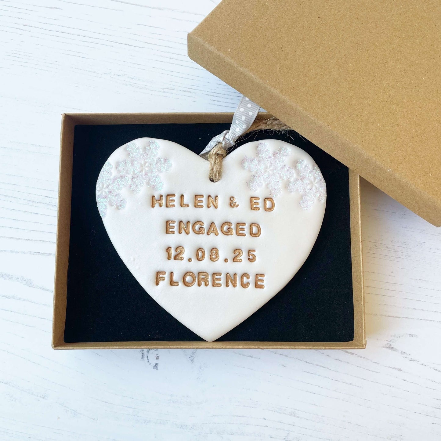 Personalised first Christmas engaged heart ornament, pearlised white clay with HELEN & ED ENGAGED 12.08.25 FLORENCE painted gold, decorated with 2 iridescent glitter snowflakes on either side of the top of the heart