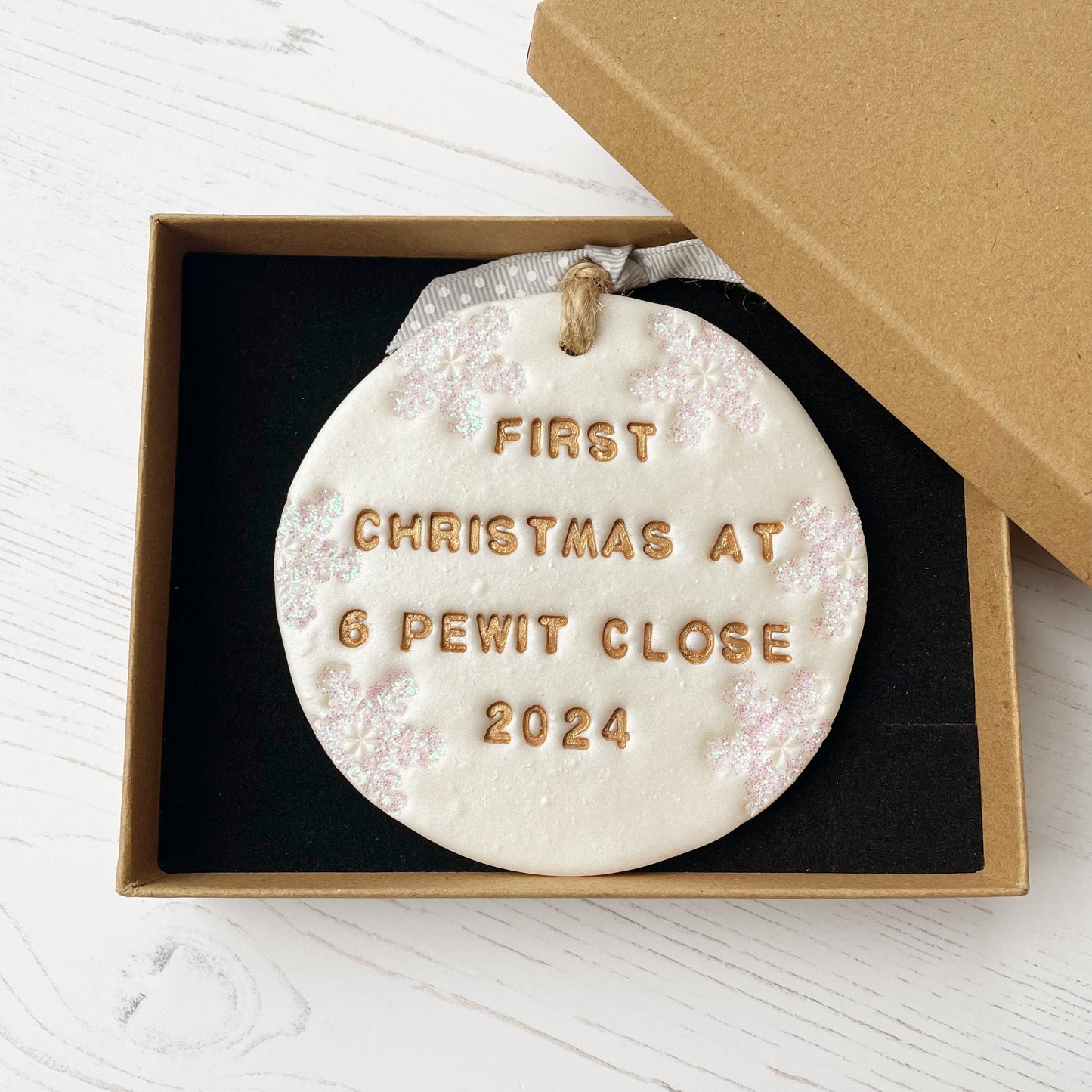 Personalised first Christmas in our new home bauble ornament, pearlised white round clay with FIRST CHRISTMAS AT 6 PEWIT CLOSE 2024 in gold paint, decorated with 3 iridescent glitter snowflakes on either side of the bauble
