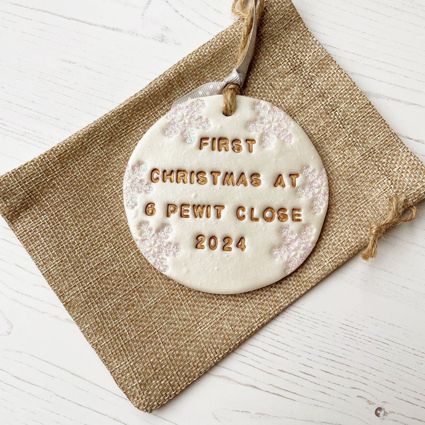 Personalised first Christmas in our new home bauble ornament, pearlised white round clay with FIRST CHRISTMAS AT 6 PEWIT CLOSE 2024 in gold paint, decorated with 3 iridescent glitter snowflakes on either side of the bauble