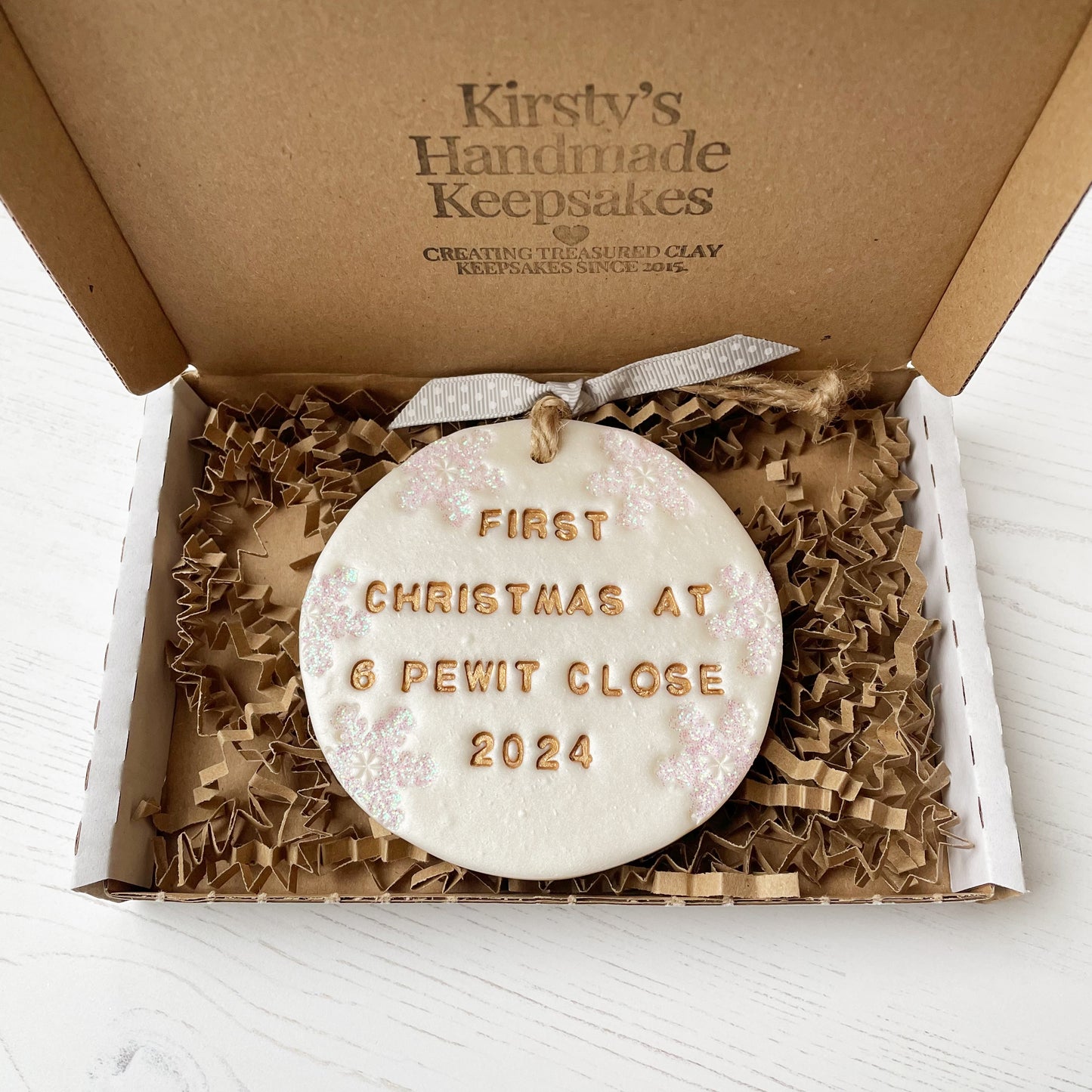 Personalised first Christmas in our new home bauble ornament, pearlised white round clay with FIRST CHRISTMAS AT 6 PEWIT CLOSE 2024 in gold paint, decorated with 3 iridescent glitter snowflakes on either side of the bauble