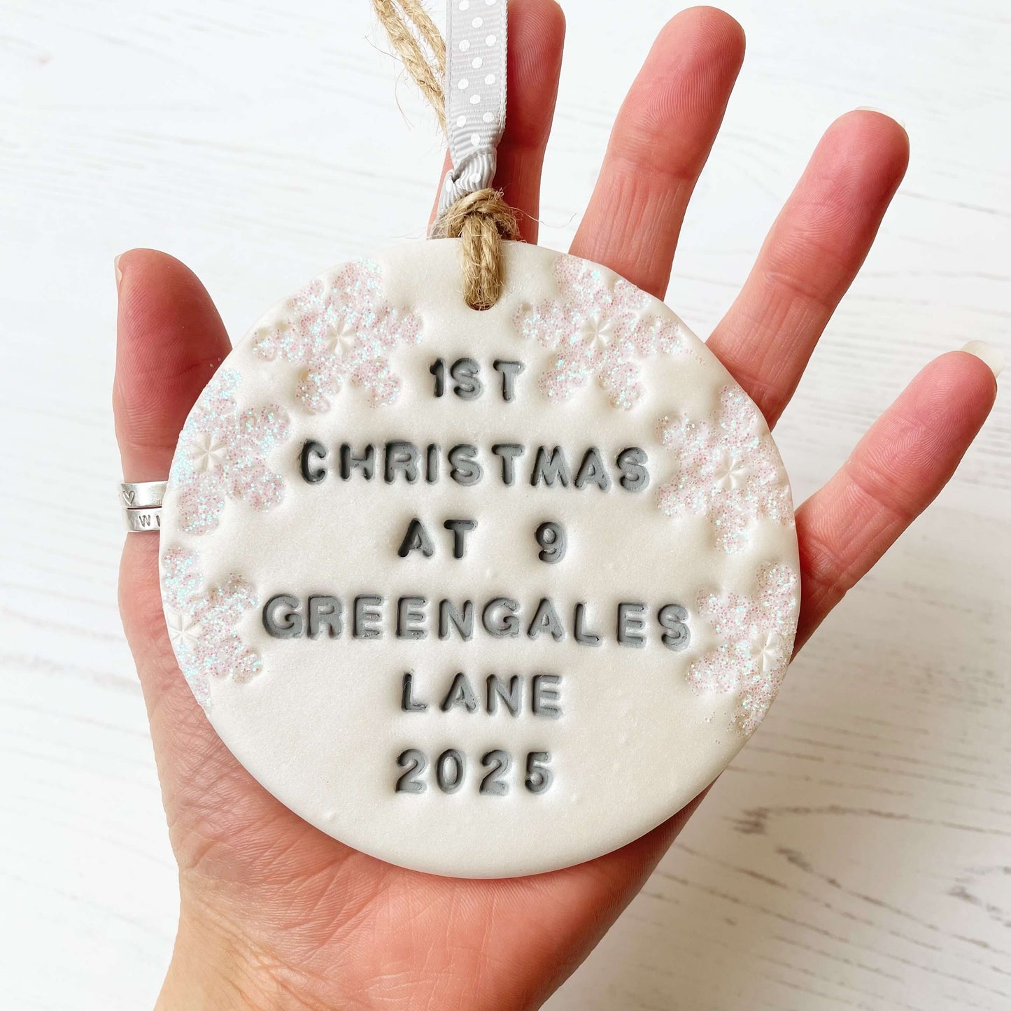 Personalised first Christmas in our new home bauble ornament, pearlised white round clay with 1ST CHRISTMAS AT 9 GREENGALES LANE 2025 in grey paint, decorated with 3 iridescent glitter snowflakes on either side of the bauble