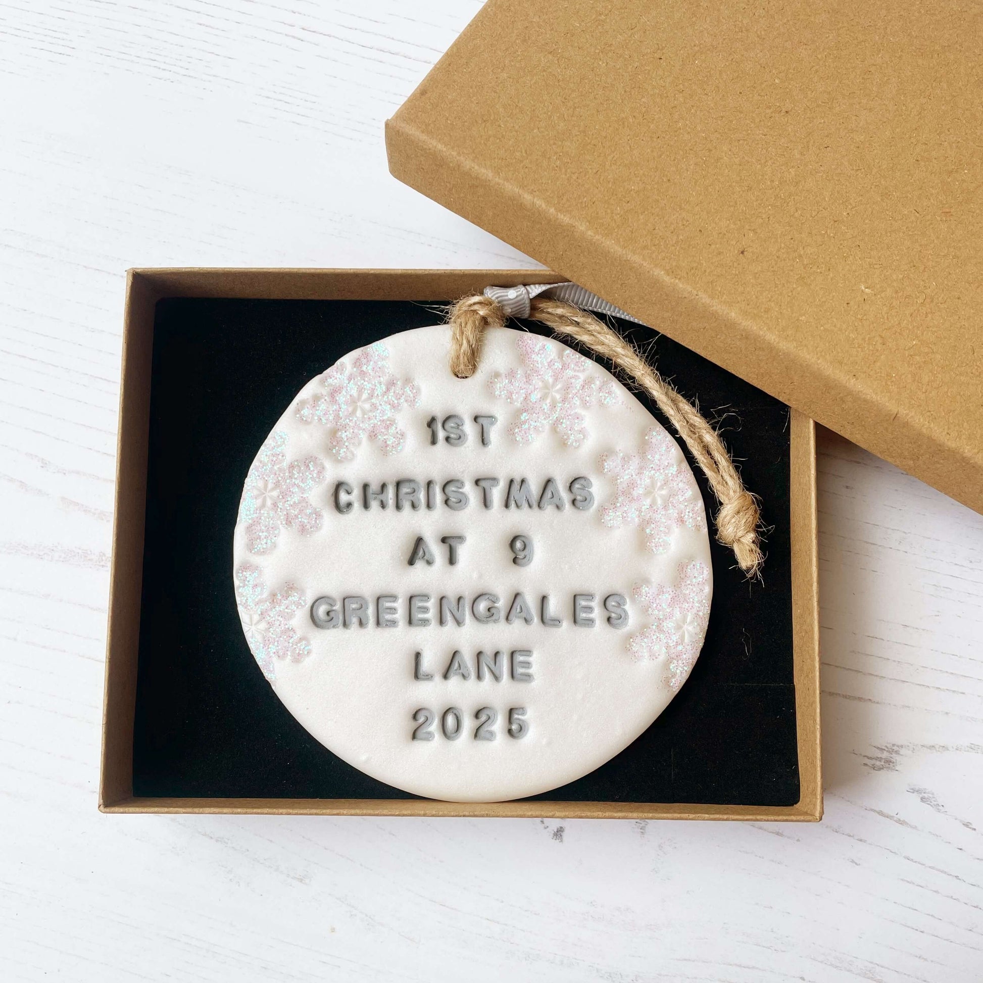 Personalised first Christmas in our new home bauble ornament, pearlised white round clay with 1ST CHRISTMAS AT 9 GREENGALES LANE 2025 in grey paint, decorated with 3 iridescent glitter snowflakes on either side of the bauble