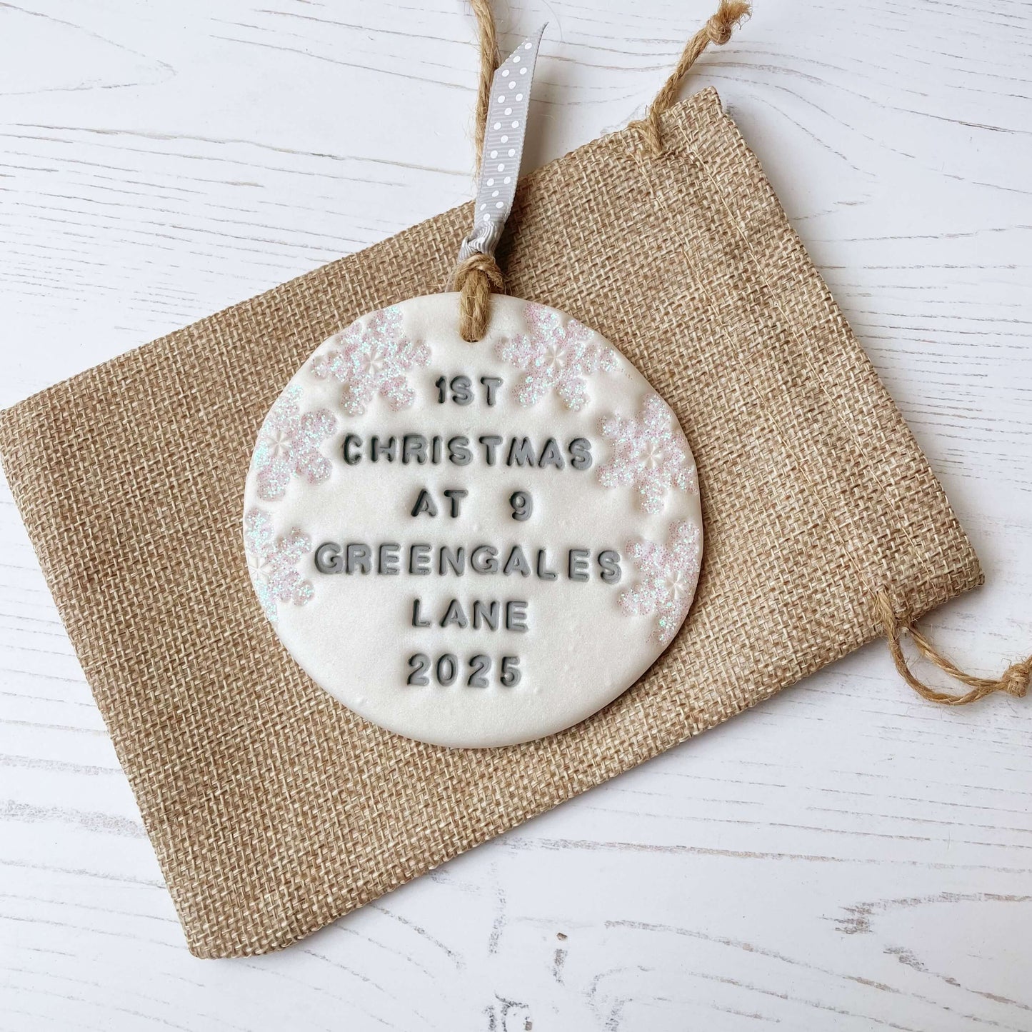 Personalised first Christmas in our new home bauble ornament, pearlised white round clay with 1ST CHRISTMAS AT 9 GREENGALES LANE 2025 in grey paint, decorated with 3 iridescent glitter snowflakes on either side of the bauble