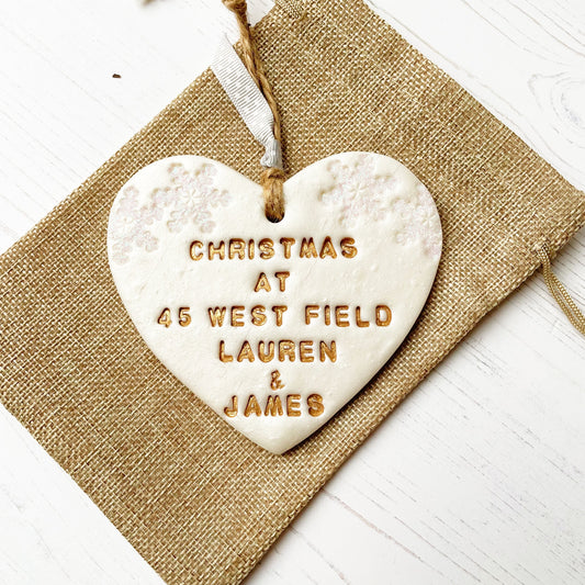 Personalised first Christmas in our new home heart ornament, pearlised white clay with CHRISTMAS AT 45 WEST FIELD LAUREN & JAMES painted gold, decorated with 2 iridescent glitter snowflakes on either side of the top of the heart