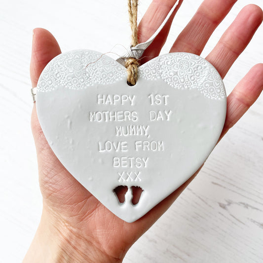 Personalised first Mother’s Day keepsake gift, grey clay hanging heart with baby feet cut out at the bottom of the heart and a white lace edge at the top of the heart, the heart is personalised with HAPPY 1ST MOTHER'S DAY MUMMY, LOVE FROM BETSY XXX