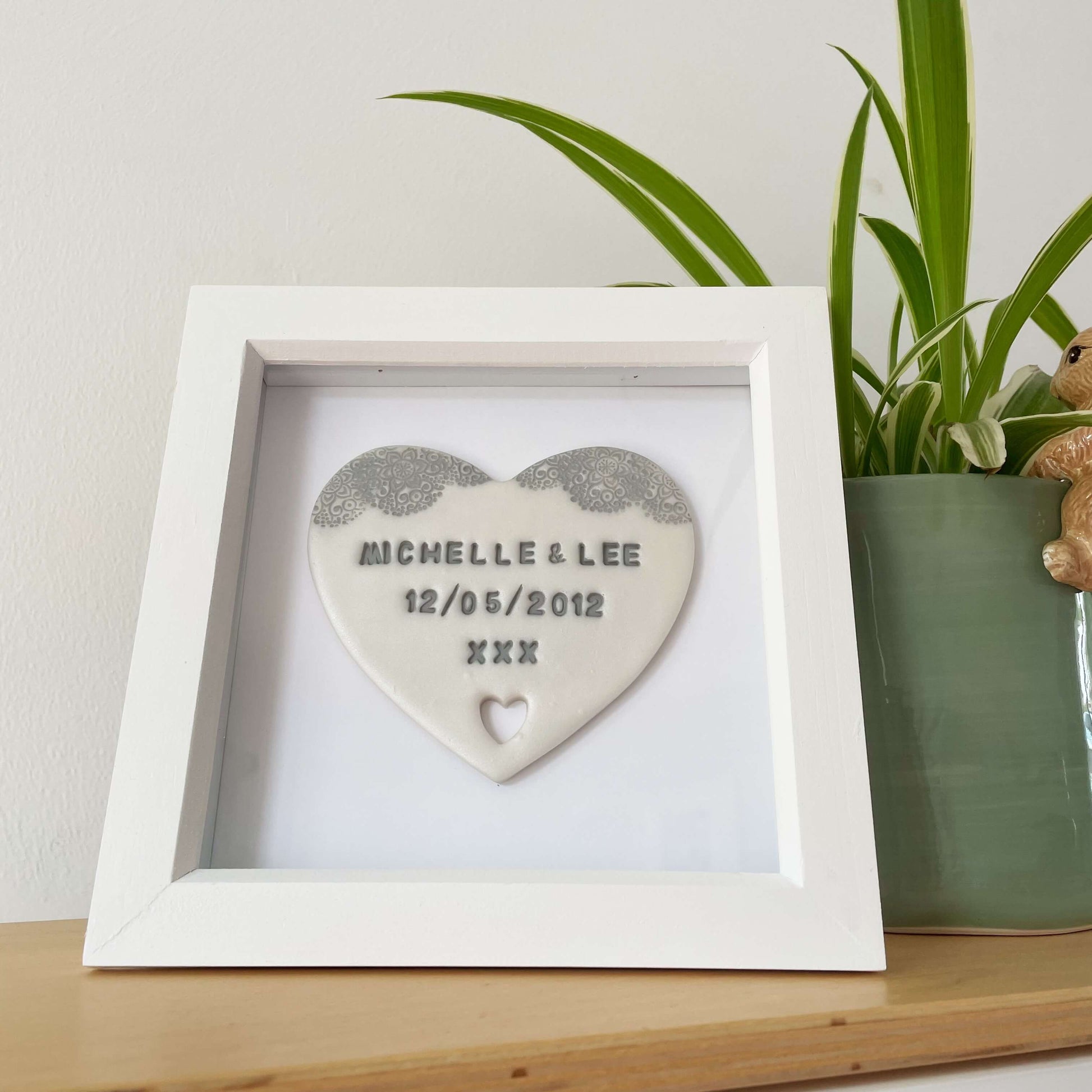 Personalised housewarming new home gift, pearlised white clay heart with a grey lace edge at the top of the heart and a heart cut out at the bottom in a white box frame, the heart is personalised with MICHELLE & LEE 12/05/2012 XXX