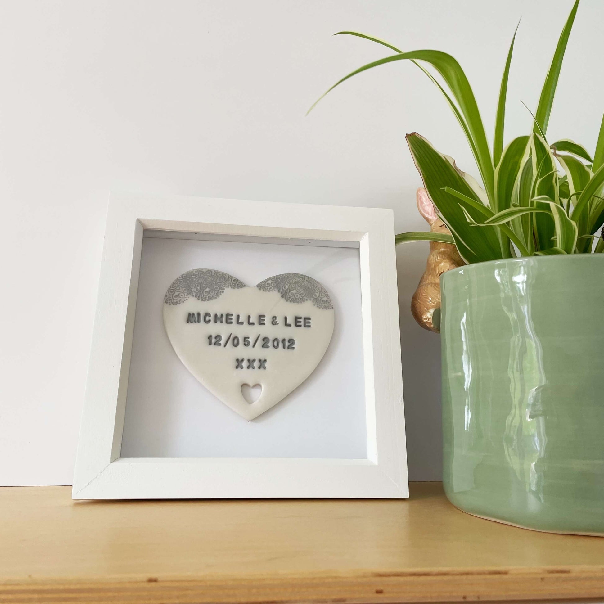 Personalised housewarming new home gift, pearlised white clay heart with a grey lace edge at the top of the heart and a heart cut out at the bottom in a white box frame, the heart is personalised with MICHELLE & LEE 12/05/2012 XXX