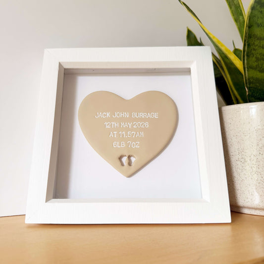 Personalised baby keepsake gift, beige clay heart with baby feet cut out at the bottom of the heart in a white box frame, the heart is personalised with the baby’s name, date of birth, weight and time