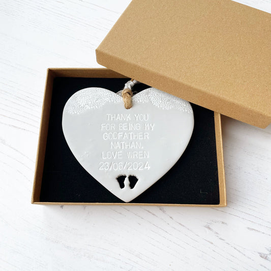 Personalised Godfather gift, grey clay hanging heart with baby feet cut out of the bottom and white lace edge at the top of the heart, the heart is personalised with THANK YOU FOR BEING MY GODFATHER NATHAN. LOVE WREN 23/06/2024 in a luxury brown Kraft gift box