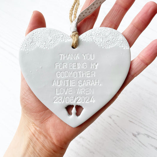 Personalised Godmother gift, grey clay hanging heart with baby feet cut out of the bottom and white lace edge at the top of the heart, the heart is personalised with THANK YOU FOR BEING MY GODMOTHER AUNTIE SARAH. LOVE WREN 23/06/2024