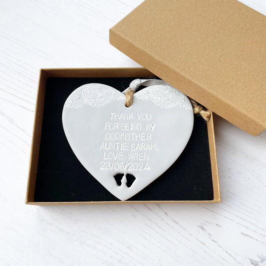 Personalised Godmother gift, grey clay hanging heart with baby feet cut out of the bottom and white lace edge at the top of the heart, the heart is personalised with THANK YOU FOR BEING MY GODMOTHER AUNTIE SARAH. LOVE WREN 23/06/2024 In a brown Kraft luxury gift box