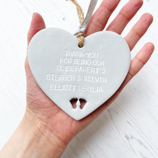 Personalised Guide parent gift, grey clay hanging heart with baby feet cut out of the bottom, the heart is personalised with THANK-YOU FOR BEING OUR GUIDEPARENT’S STEPHEN & KELVIN. ELLIOTT & EMILIA