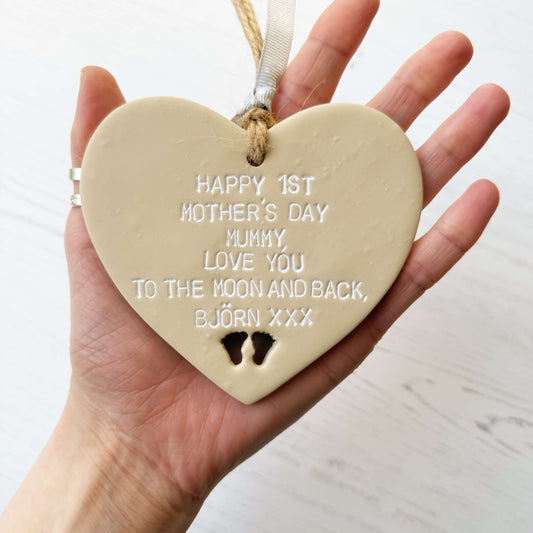 Personalised 1st Mother’s Day gift, beige clay hanging heart with baby feet cut out at the bottom of the heart, the heart is personalised with HAPPY 1ST MOTHER’S DAY MUMMY, LOVE YOU TO THE MOON AND BACK, BJÖRN XXX